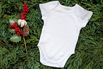White blank template bodysuit romper lying on fir tree branches near pine cone with cotton and red...