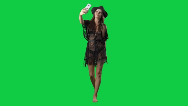 Pretty influencer summer girl in tunic walking and vlogging with smart phone. Full body on green screen chroma key background