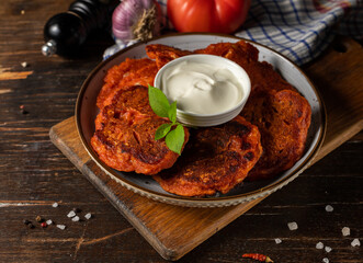 Carrot or tomato cutlets with sauce on a gray plate. Close-up on a dark wooden table, with cooking ingredients in the background.