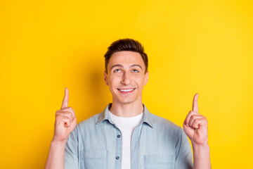 Portrait of young smiling good mood man look up advertising product point fingers copyspace...