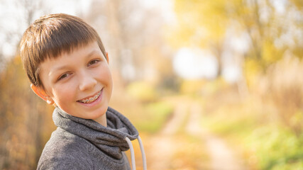 A cheerful teenager with braces on his teeth walks down the street on a bright day. Horizontally.