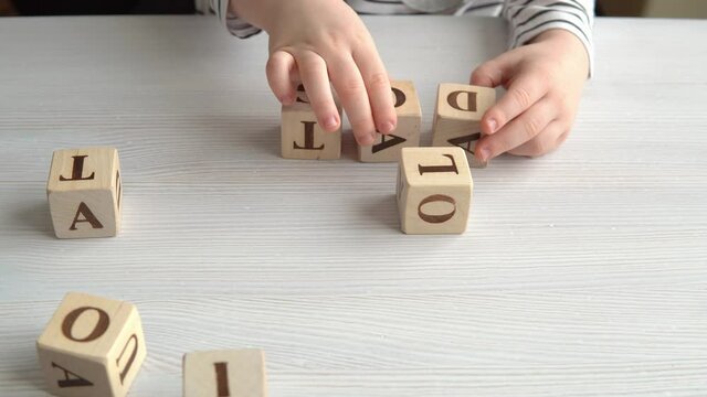 Little boy learn letters, spelling, reading and writing, play with wooden cubes on table, preschool education, alphabet learning concept.