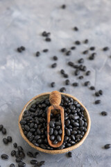 Fototapeta na wymiar Bowl full of dried black beans with a scoop on grey table close up