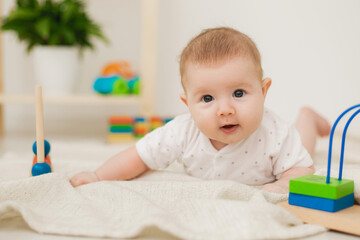 cute baby is lying on his stomach on a gray linen blanket and playing with colored educational toys. products for children. concept of a happy childhood and motherhood. child care. space for text