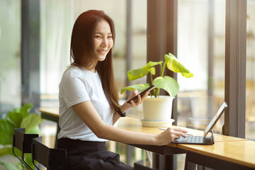 Female in casual outfits sits in co-working space, working on tablet and mobile phone.
