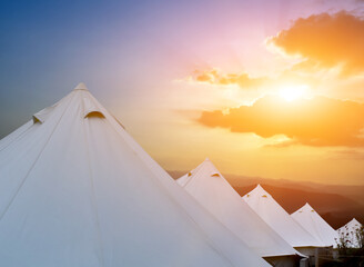 Fototapeta na wymiar Row of white pyramid tents on high hills for travellers with the sunset background. Soft and selective focus.