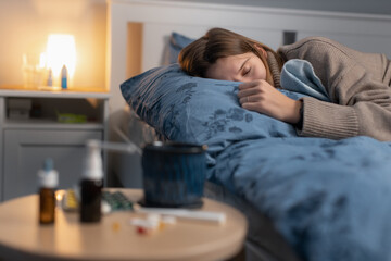 Obraz premium Illness girl sleeping in bed. Near table with various medicines and pills. Woman got the flu or a cold. Medications for nasal congestion and to reduce fever. Selective focus on female. Healthcare.