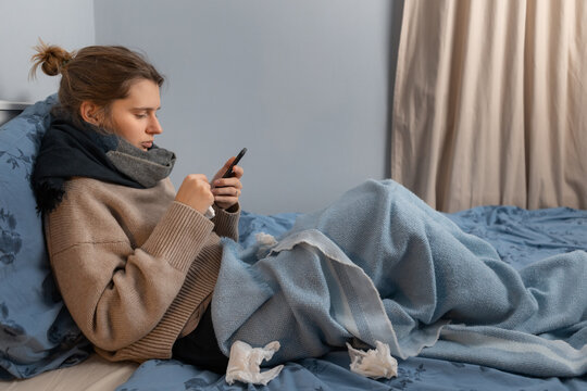 Sickness handsome woman in beige sweater sitting in bed and searching medicines delivery in internet. Online purchase of medicines. Girl searching in web disease treatment by the symptoms. Copy space.