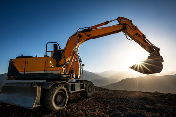 Excavator is working on the hill at sunset. Excavators are heavy construction equipment consisting...