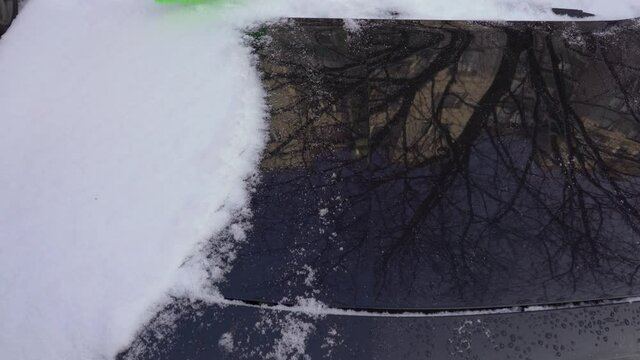Winter cleaning concept. Person removes thick layer of fresh white snow covered his black car thickly outdoors