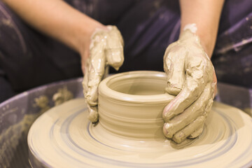 Pottery artist hands molding clay vase on pottery wheel at art workshop.