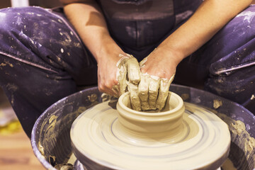 Pottery artist hands molding clay vase on pottery wheel at art workshop.