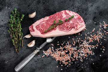 Raw new york strip steak on a butcher table with salt and thyme. Black background. Top view