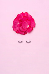 Creative woman face made of eyelashes and rose petals hair on the pink background. Minimal beauty concept. Makeup creative concept. Flat lay.