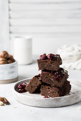Chocolate vegan brownie with cherries and nuts on a plate. Homemade cakes on a light background