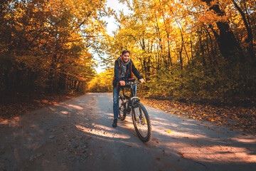 A man on a bicycle rides along the road in the autumn forest in the evening at sunset