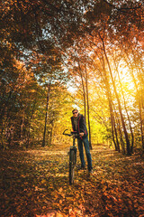 Fototapeta premium Man on a bike in the autumn forest in the evening at sunset