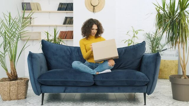 Disappointed young woman unpacking huge carton box, looking inside. Unsatisfied customer opening cardboard box with online store order, bad shipping delivery service