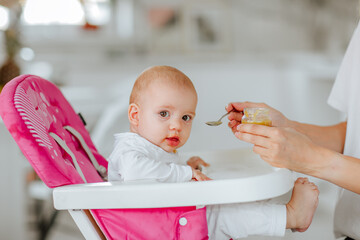 Mother in white shirt feeds her newborn baby girl by spoon