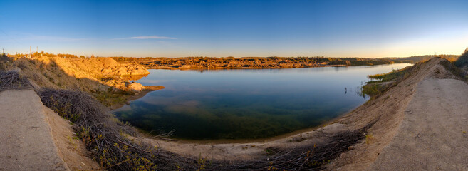 Full seamless panorama 180 angle view near quarry flooded with water for sand extraction mining in the evening sun. Landscape of abandoned quarry looks like Mars. 