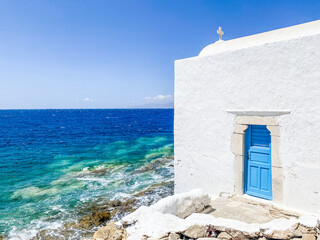beautiful details of a typical greek orthodox church with white wall and blue door, close to the aegean sea