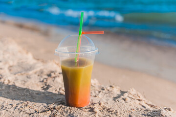 Colored chilled non-alcoholic cocktail stands on the sand of the sea beach against the background of water and sky