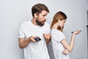 man and woman in white T-shirts with phones in their hands light background