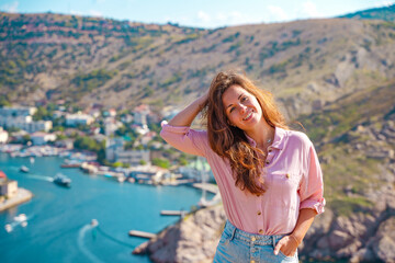 A young beautiful woman admires the picturesque landscape with a view of Balaclava with yachts and a colorful bay in summer. Postcard view of the tourist Crimea.