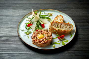 Delicious beef tartare with yolk and croutons on a plate. wood background. Selective focus