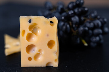 Pieces of aromatic parmesan and black raisins grapes on a dark background. Wine plate.