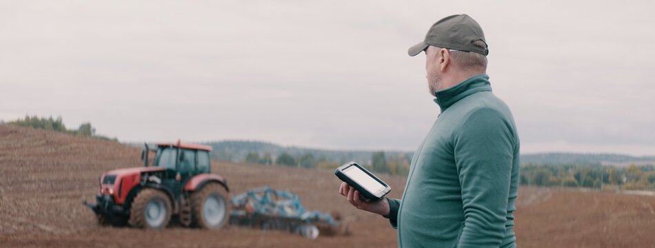 Portrait of 50s Caucasian male farmer using a tablet while standing in the field. Cloud technology for agriculture
