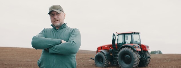 Hero shot portrait of 50s farmer posing against tractor early in the morning in the field