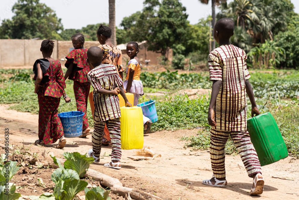 Wall mural group of black african children carrying empty water containers on their way home from the village w