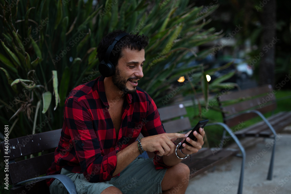 Wall mural Young man listening to music. Urban fashion man with headphones enjoying the city