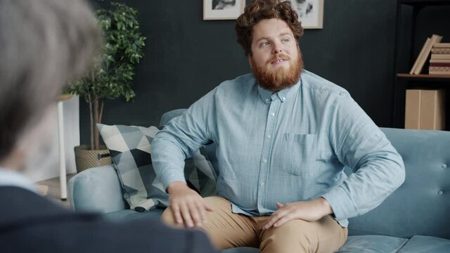 Adult man with strange behavior is talking to therapist during session in modern office while doctor is listening giving advice. People and psychotherapy concept.