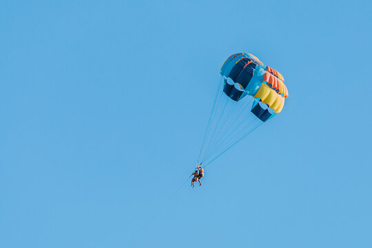 Extreme sports and exciting rest activity. Vacationing tourists fly on a parashute in blue sky background