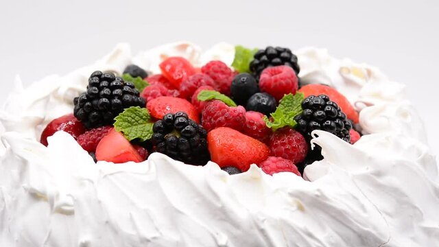 Delicious Pavlova cake with meringue and fresh berries rotating on white background