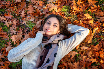 Portrait of a beautiful, brunette woman lying under october sunshine in colorful autumn leafes in a park