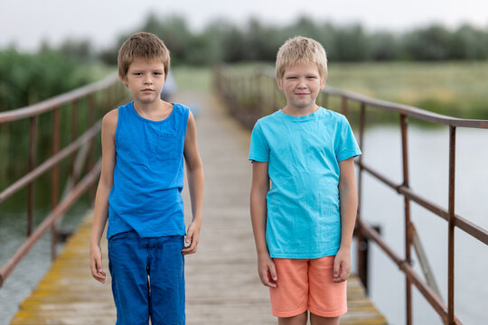 Two boys in colorful clothes stand on bridge over river in village
