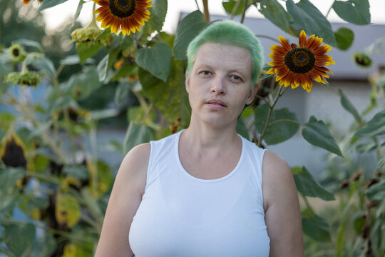 woman with green hair stands on plot with sunflowers