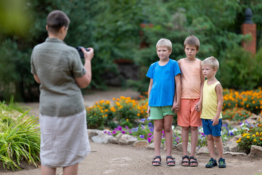 woman in military uniform takes pictures of her children in colorful clothes in park against background of flowers