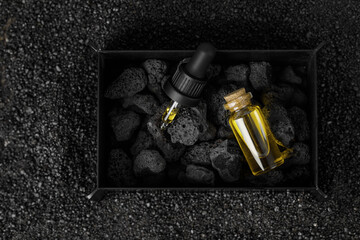 Essential oil in glass bottle for aromatherapy and mineral diffuser with volcanic stones in iron metal box on black sand background. Aromatherapy, spa, beauty treatment and wellness concept.