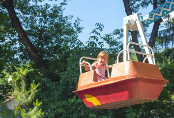 Little sad girl child todler sitting on old child ferris wheel in amusement park	