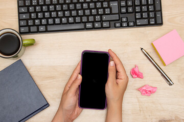 businesswoman holding phone and computer keyboard, coffee cup, sticky note,book, and pen on the desk