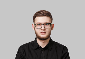 Obraz premium Young serious man with stylish neat beard, wearing a black shirt and in glasses