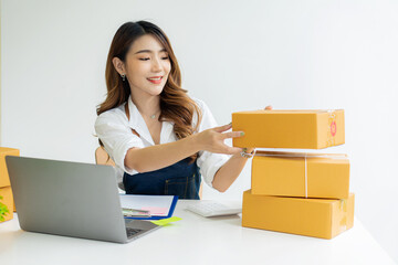 Beautiful Asian freelance SME online shopping business working on laptop computer with parcel box at home desk. delivery concept young woman owning a small business online shopping at home Take note o