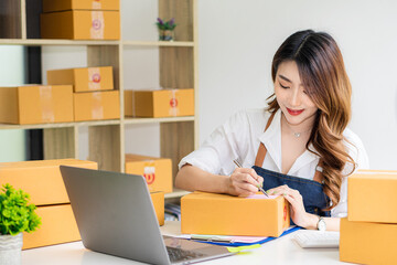 Fototapeta na wymiar Beautiful Asian freelance SME online shopping business working on laptop computer with parcel box at home desk. delivery concept young woman owning a small business online shopping at home Take note o