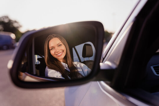 Photo of sweet cute young lady dressed white shirt smiling looking back mirror driving automobile outdoors urban route