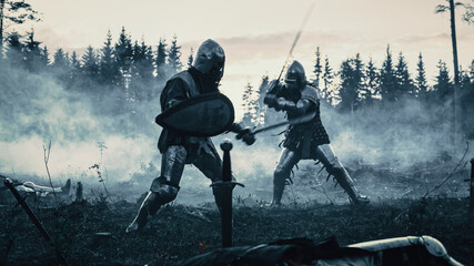 Dark Age Battlefield: Two Armored Medieval Knights Fighting with Swords. Battle of Armed Warrior Soldiers, Killing Enemy in Mysterious Forest. Cinematic Smoke, Mist, Light in Historic Reenactment - obrazy, fototapety, plakaty