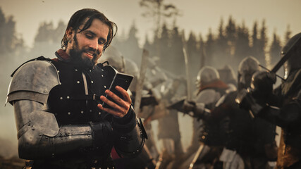 Portrait of Handsome Medieval Knight Using Smartphone on Battlefield, Smiling. Fun Concept:...